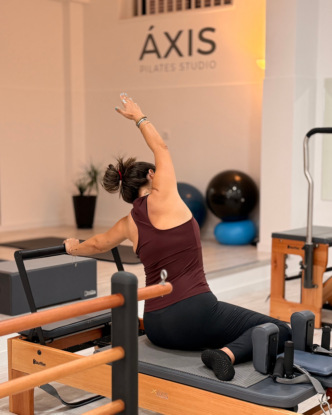 Aluna em extensão de coluna no reformer, parede ÁXIS ao fundo